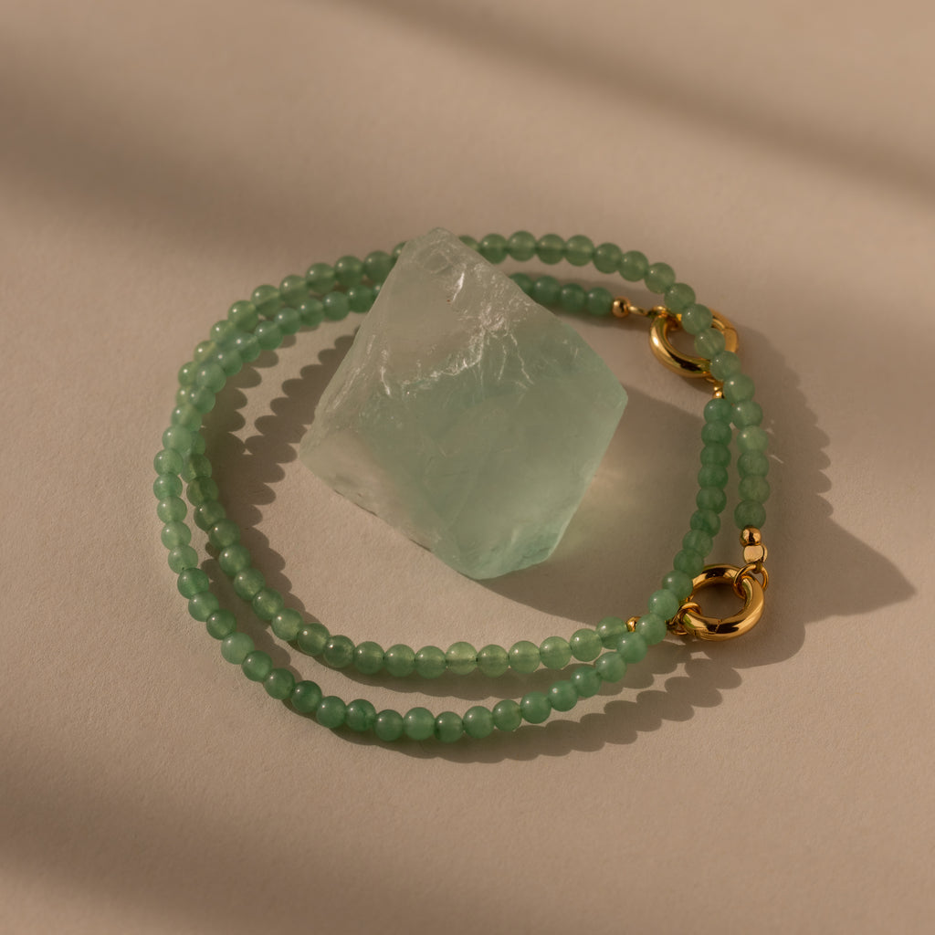 The Beaded Jade Clasp Bracelet features green beads and gold clasps, beautifully highlighting a translucent jade stone—an elegant accessory to pair with your favorite jewelry.