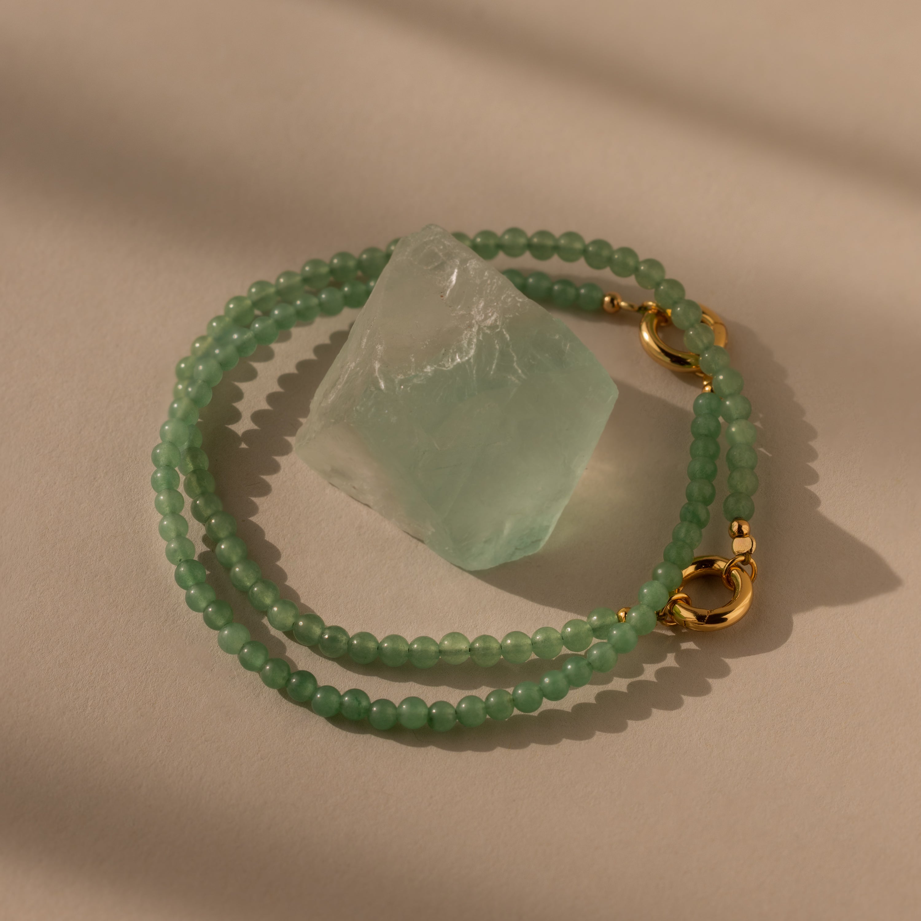 The Beaded Jade Clasp Bracelet features green beads and gold clasps, beautifully highlighting a translucent jade stone—an elegant accessory to pair with your favorite jewelry.