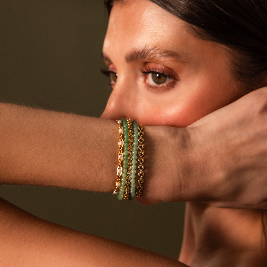 A woman poses with her arm raised, highlighting the Beaded Jade Clasp Bracelet featuring layered gold and green jade beads.