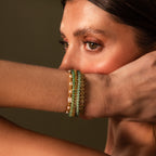 A woman poses with her arm raised, highlighting the Beaded Jade Clasp Bracelet featuring layered gold and green jade beads.
