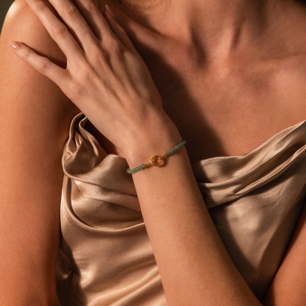 A woman wearing a gold satin dress showcases the Beaded Jade Clasp Bracelet on her wrist.
