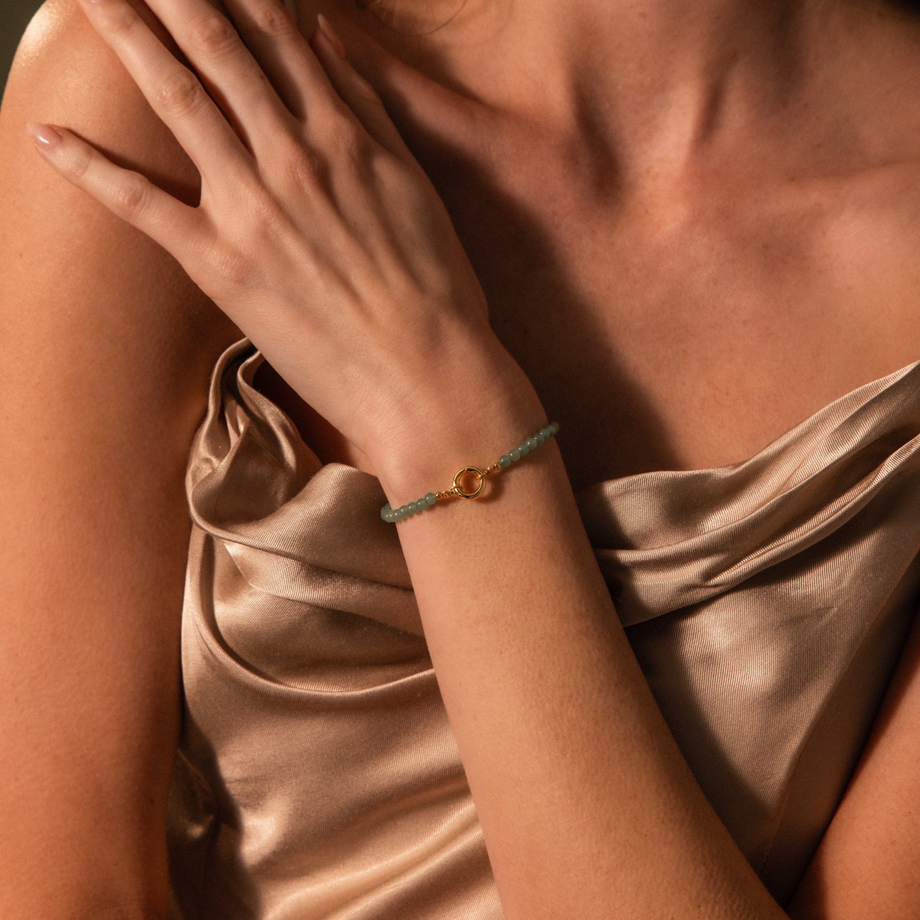 A woman wearing a gold satin dress showcases the Beaded Jade Clasp Bracelet on her wrist.
