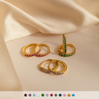 Vera Pave Birthstone Huggies, gold hoop earrings with vibrant birthstones, are shown on cream fabric in natural light.