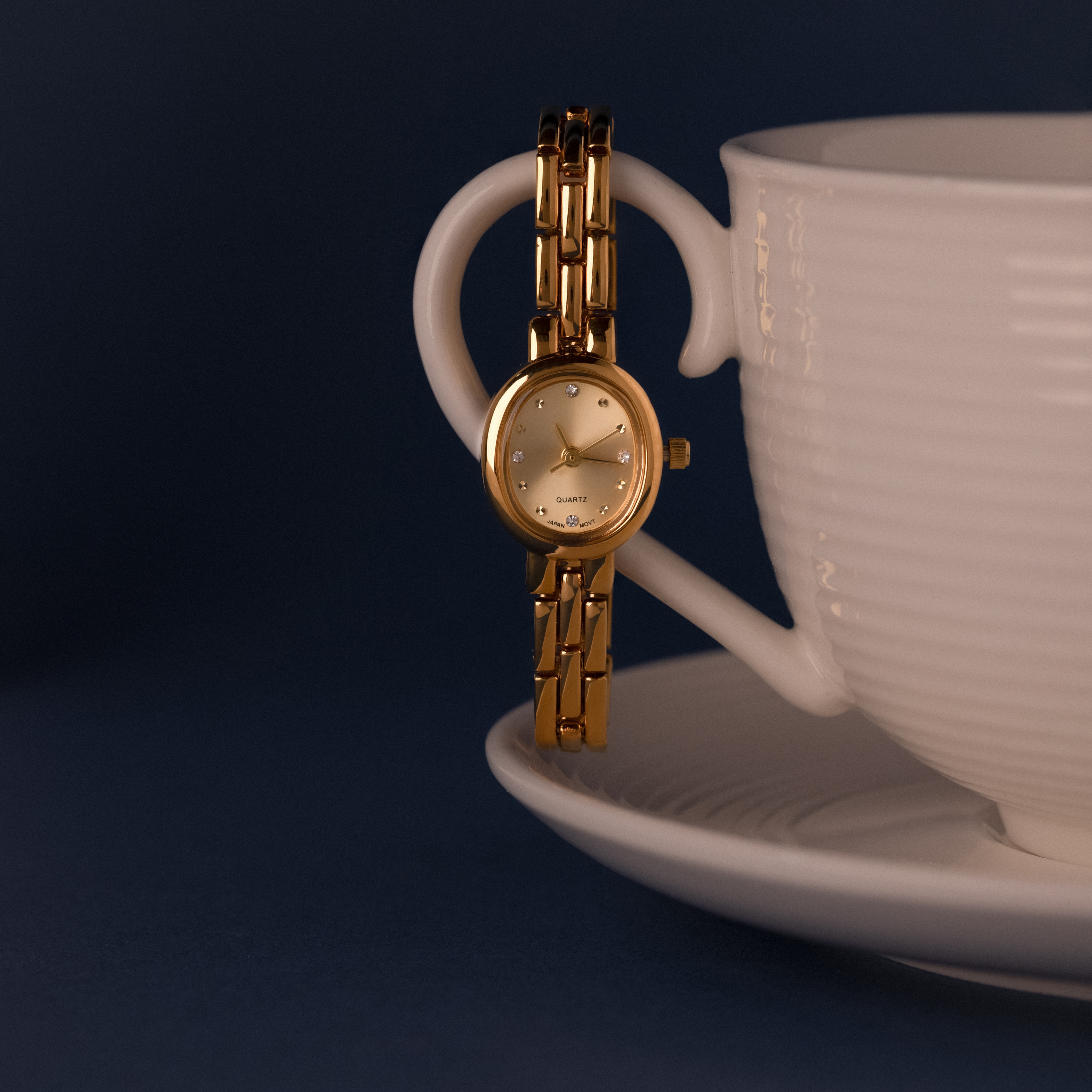 Our Cobblestone Timepiece watch laid on the handle of a teacup against a blue background