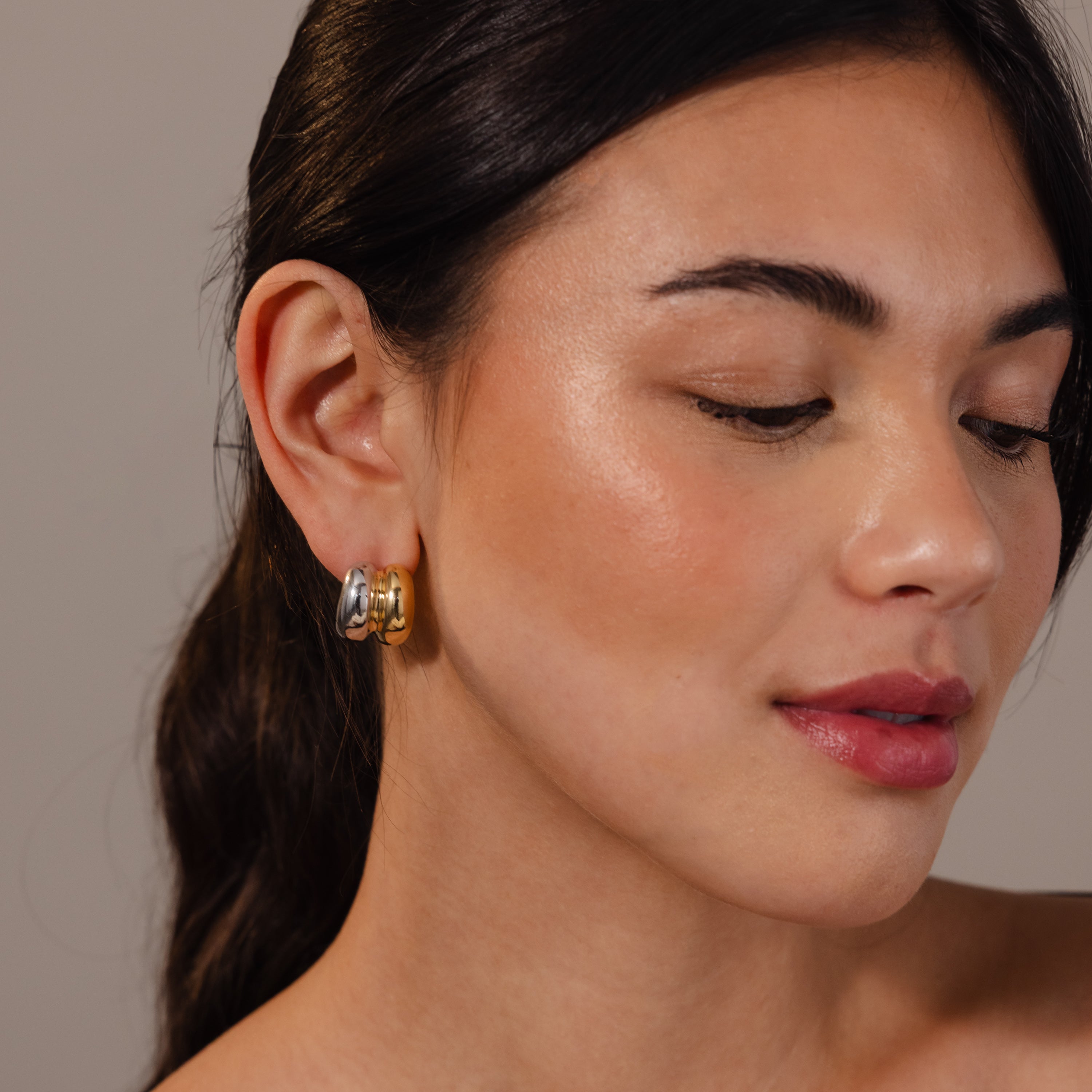 Woman with smooth skin and dark hair wears Mixed Metal Puff Studs—chunky, two-tone gold and silver earrings that showcase a bold, minimal jewelry style.