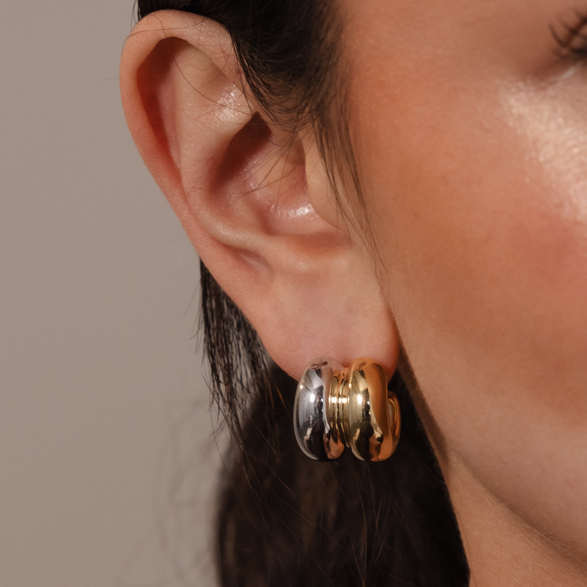 Close-up of a person’s ear wearing chunky gold and silver hoops, styled with the Mixed Metal Puff Studs for a modern, minimal jewelry look. Perfect for fans of the Mixed Metal Puff Studs.