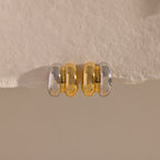 Mixed Metal Puff Studs—one silver, one gold—rest side by side on a textured beige surface. Perfect for fans of modern earrings and minimal jewelry.
