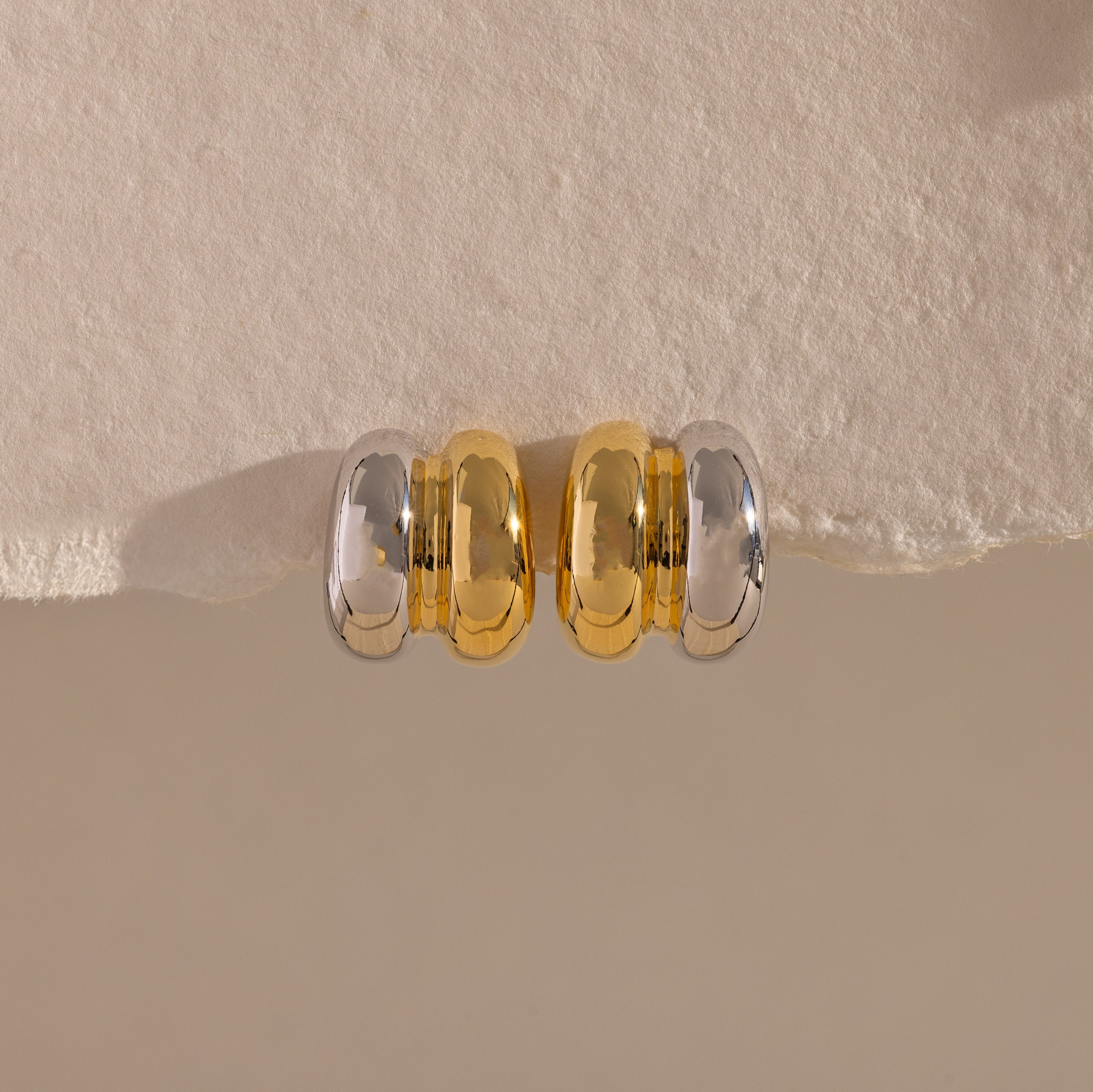 Mixed Metal Puff Studs—one silver, one gold—rest side by side on a textured beige surface. Perfect for fans of modern earrings and minimal jewelry.
