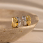 The Mixed Metal Puff Studs, featuring bold gold and silver tones, sit atop a smooth stone surface—perfect for fans of minimal jewelry.