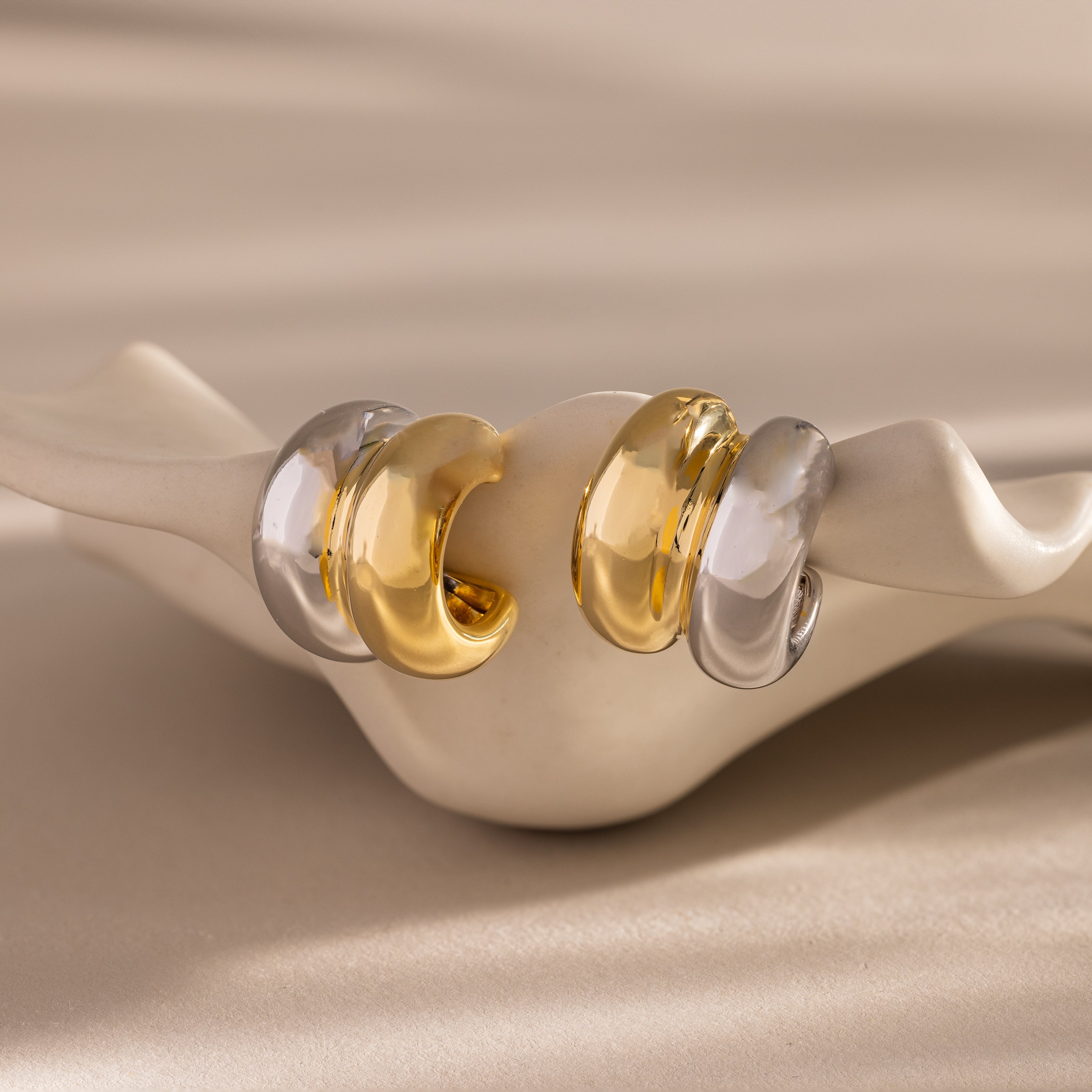 The Mixed Metal Puff Studs set features two pairs of chunky, modern earrings in gold and silver, displayed on a wavy ceramic holder—ideal for minimal jewelry lovers.