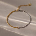 The Mixed Metal Knot Bracelet features two-tone gold and silver snake chains, a knot detail, and a heart charm—ideal for modern minimalists.