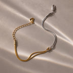 The Mixed Metal Knot Bracelet features gold and silver chains in a two-tone minimalist design, styled as a knot and displayed on a light, textured surface with soft shadows.