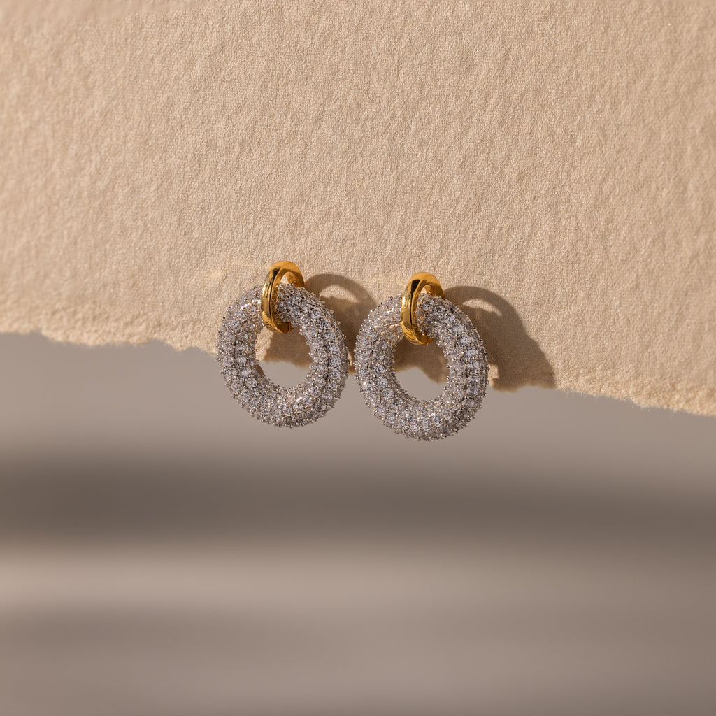 Mixed Metal Pave Circle Studs adorned with sparkling stones, displayed on a textured beige surface.