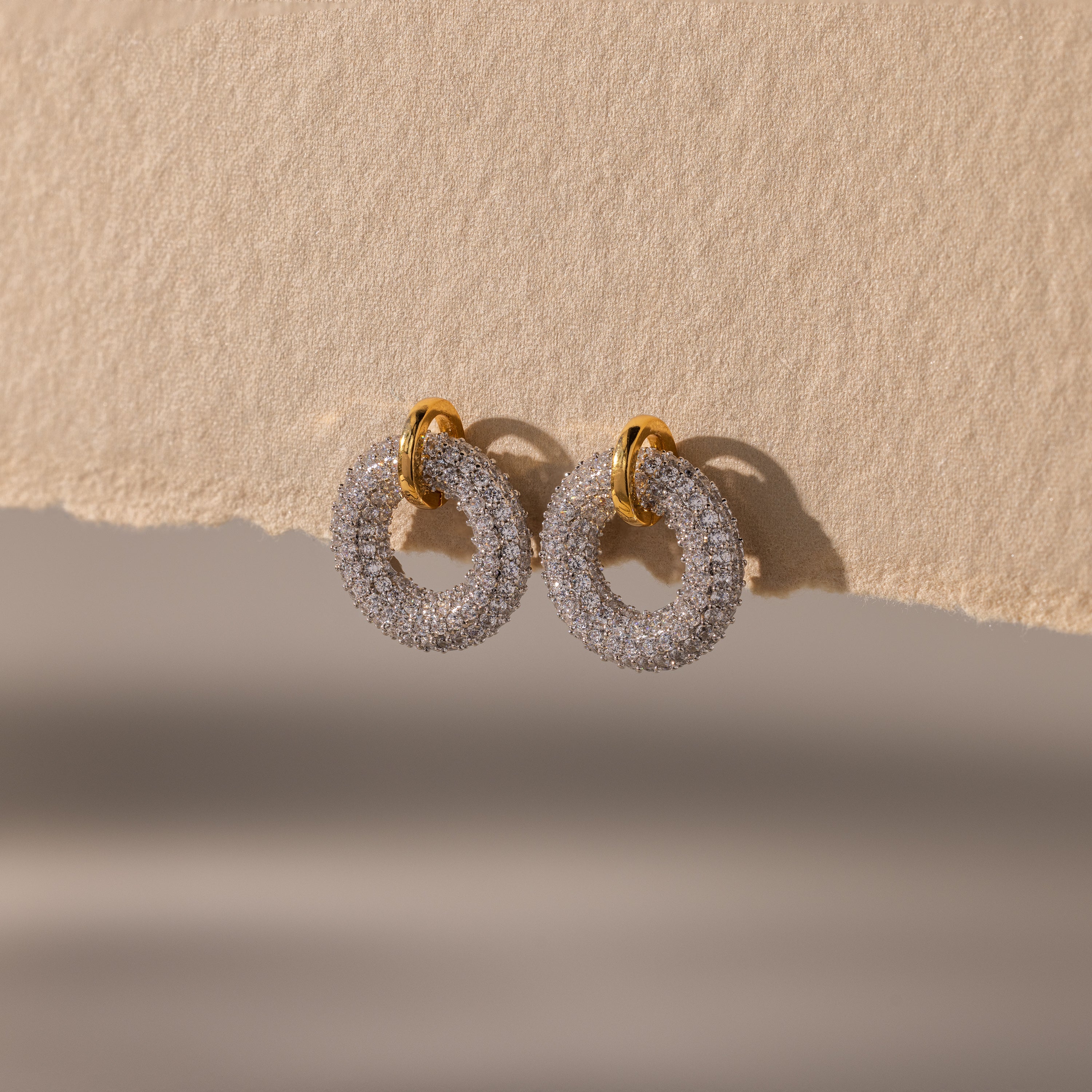 Mixed Metal Pave Circle Studs adorned with sparkling stones, displayed on a textured beige surface.