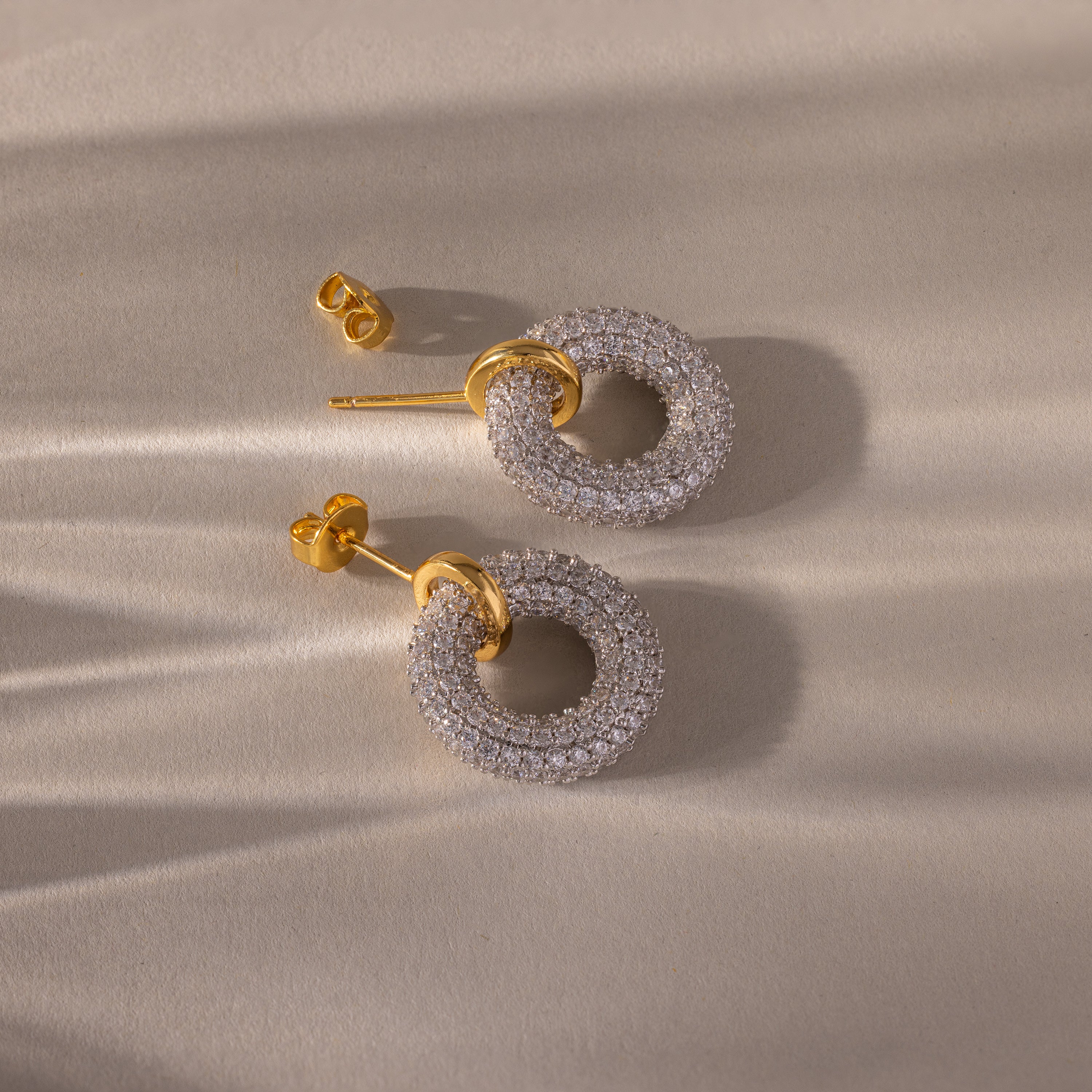 Mixed Metal Pave Circle Studs displayed on a beige surface, casting delicate shadow patterns.