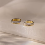 Half Pave Huggies in Mixed Metal, featuring a row of sparkling CZ diamonds, displayed on a light, glossy stone surface.