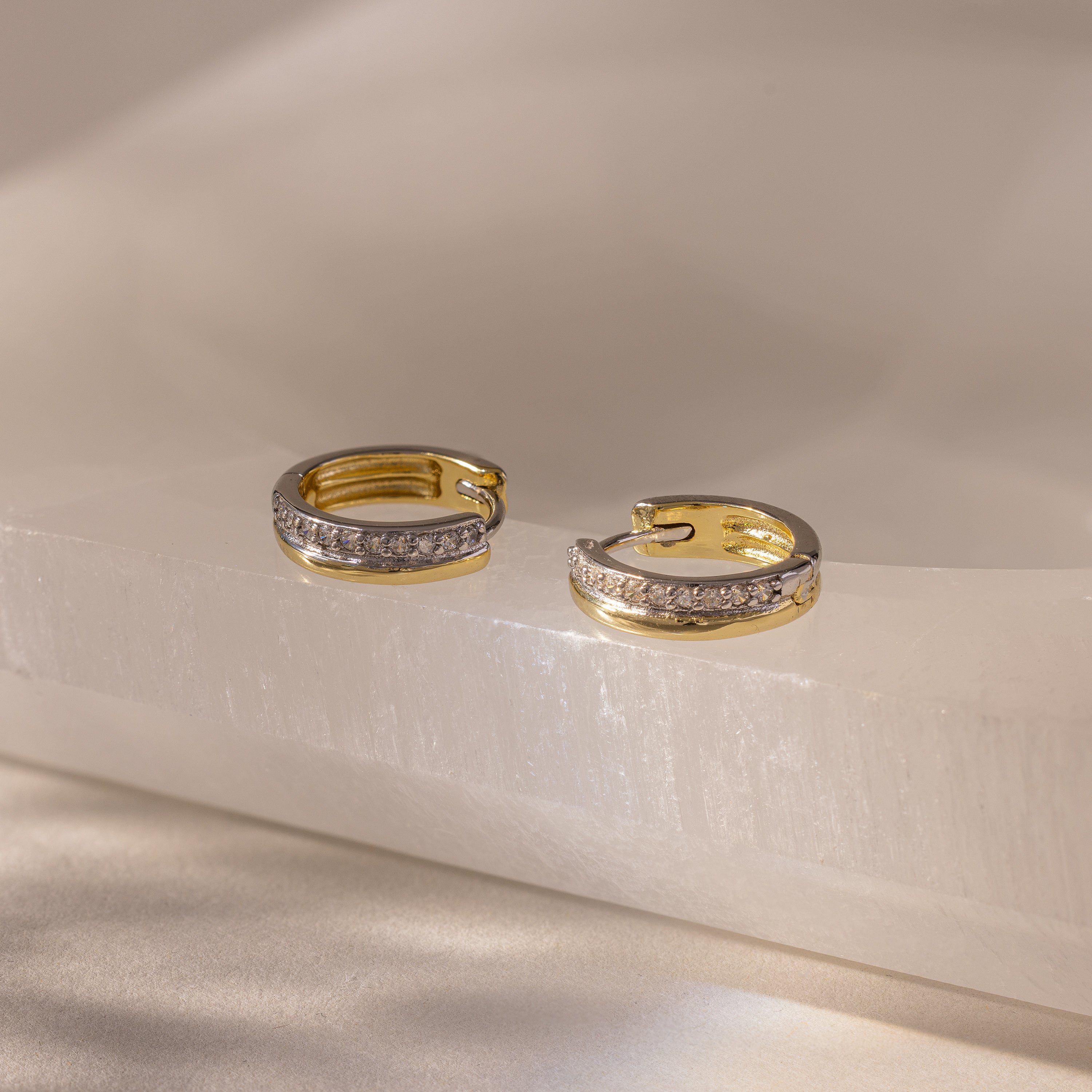 Half Pave Huggies in Mixed Metal, featuring a row of sparkling CZ diamonds, displayed on a light, glossy stone surface.