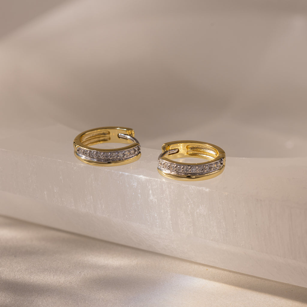 Half Pave Huggies in 18K Gold, featuring a row of sparkling CZ diamonds, are displayed on a smooth, light-colored surface.