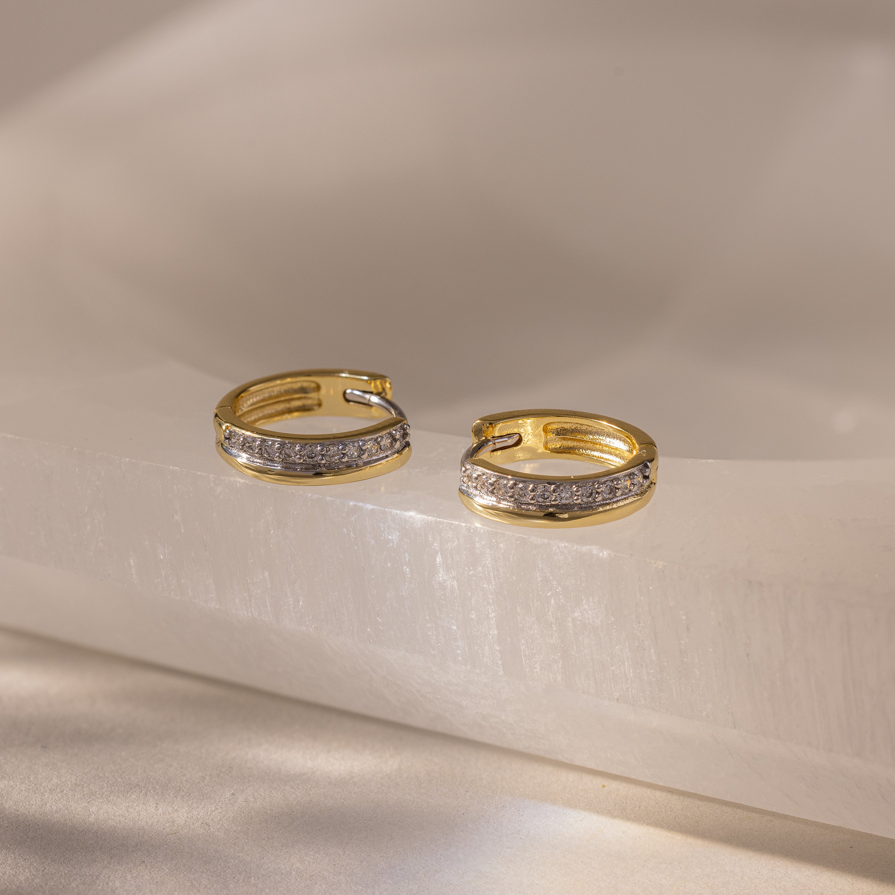 Half Pave Huggies in 18K Gold, featuring a row of sparkling CZ diamonds, are displayed on a smooth, light-colored surface.