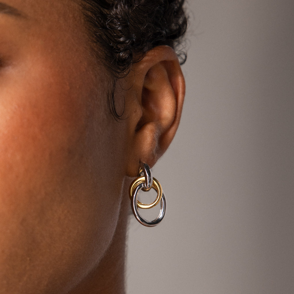 Close-up of a person's ear wearing Mixed Metal Linked Earrings—contemporary gold and silver double hoops—set against a neutral background.