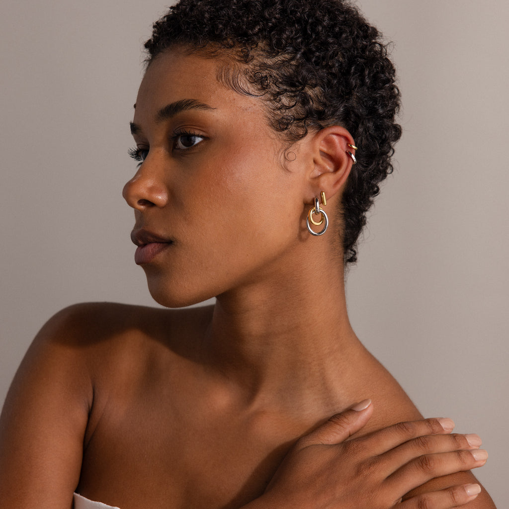 Woman with short curly hair wearing Mixed Metal Linked Earrings in gold and silver, looking left with her hand resting on her shoulder.