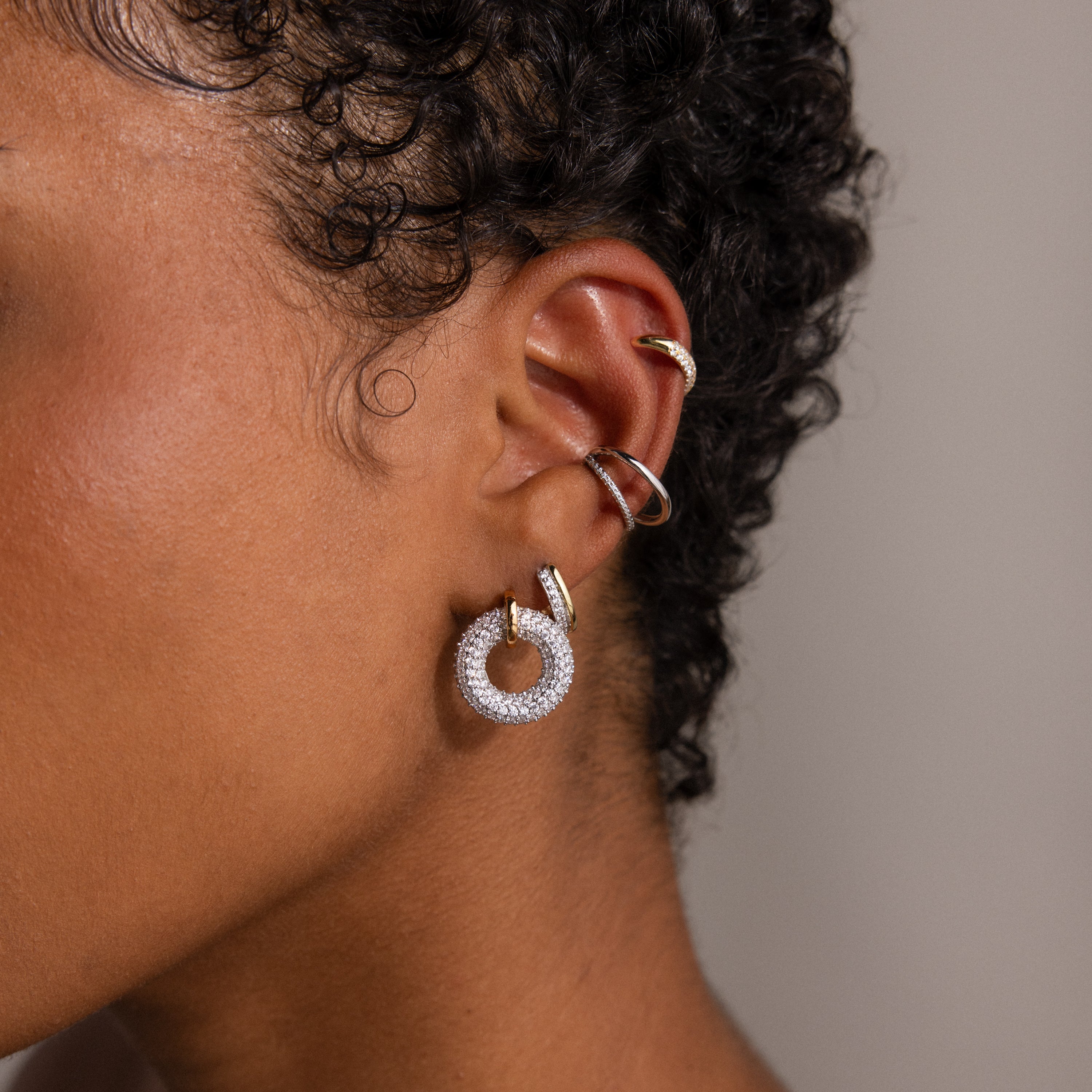 A close-up of an ear wearing multiple earrings, including the sparkling Mixed Metal Pave Circle Studs and elegant gold loops.