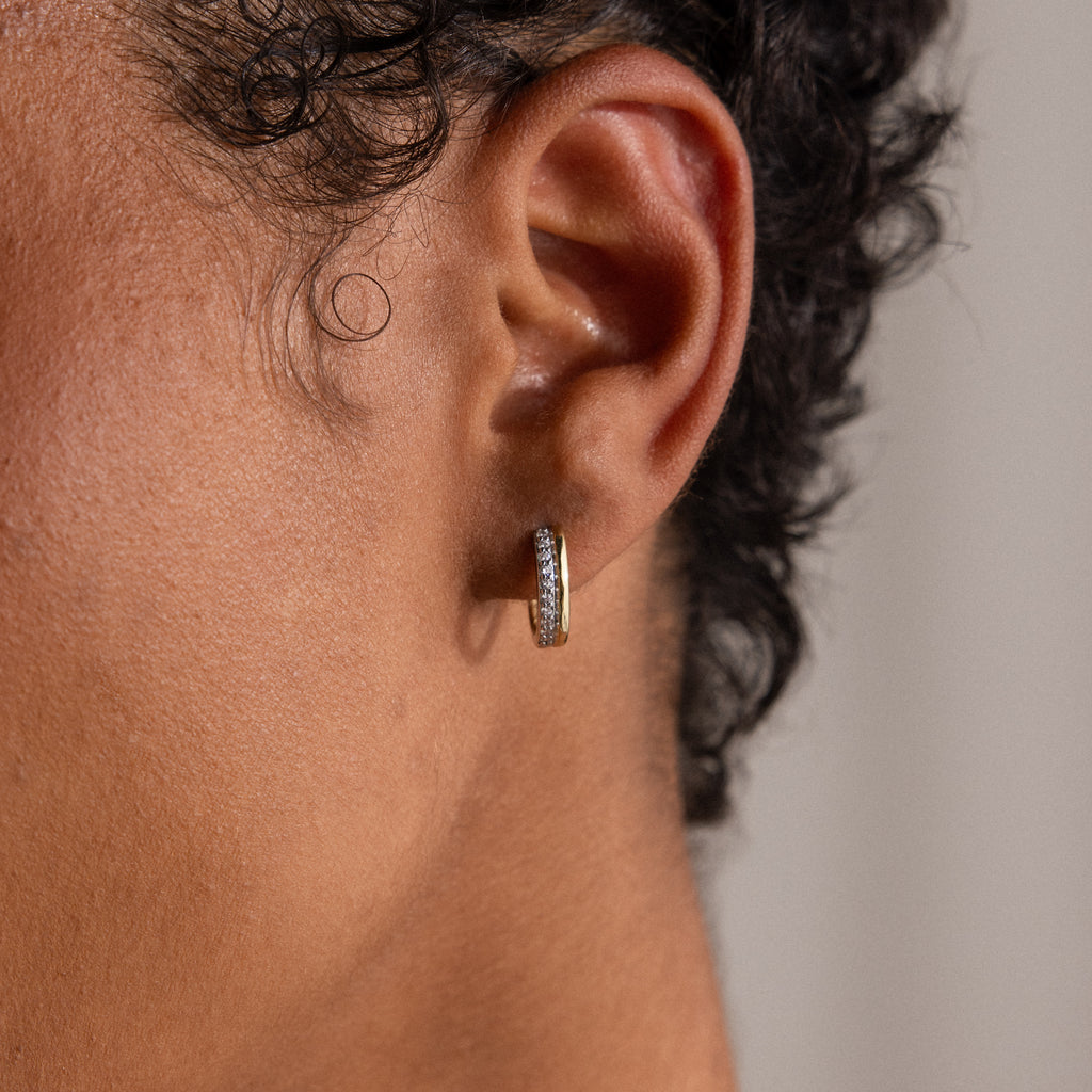 A close-up of a person with short curly hair wearing the Half Pave Huggies earring, featuring sparkling CZ diamonds and a textured design.