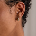 A close-up of a person with short curly hair wearing the Half Pave Huggies earring, featuring sparkling CZ diamonds and a textured design.