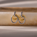 Two pairs of Mixed Metal Linked Earrings, featuring gold and silver tones, rest on a smooth beige stone surface, highlighting their contemporary style ideal for mixing metals.