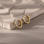 Half Pave Huggies in 18K Gold with embedded CZ diamonds displayed on a textured beige tile surface.