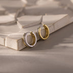Half Pave Huggies, gold or silver earrings with delicate CZ diamonds, displayed on a textured beige surface.