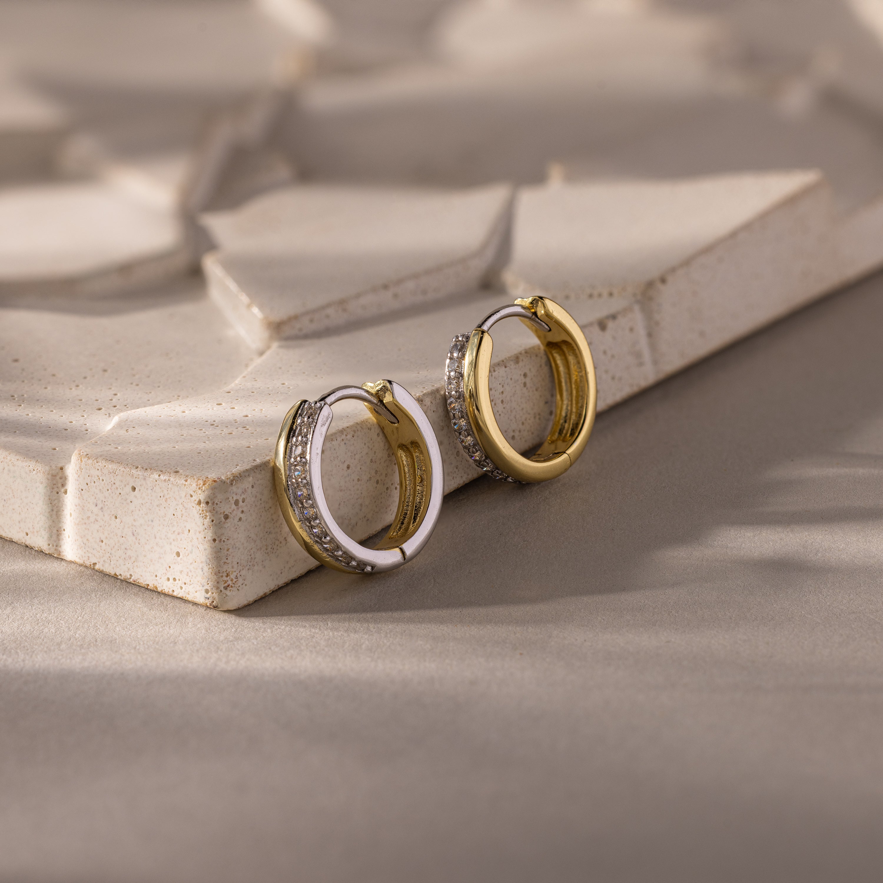 Half Pave Huggies, gold or silver earrings with delicate CZ diamonds, displayed on a textured beige surface.