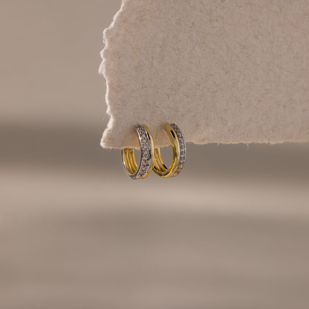 Two small Half Pave Huggies in Mixed Metal with embedded CZ diamonds hang on the edge of a textured, off-white surface.