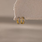 Two small Half Pave Huggies in Mixed Metal with embedded CZ diamonds hang on the edge of a textured, off-white surface.