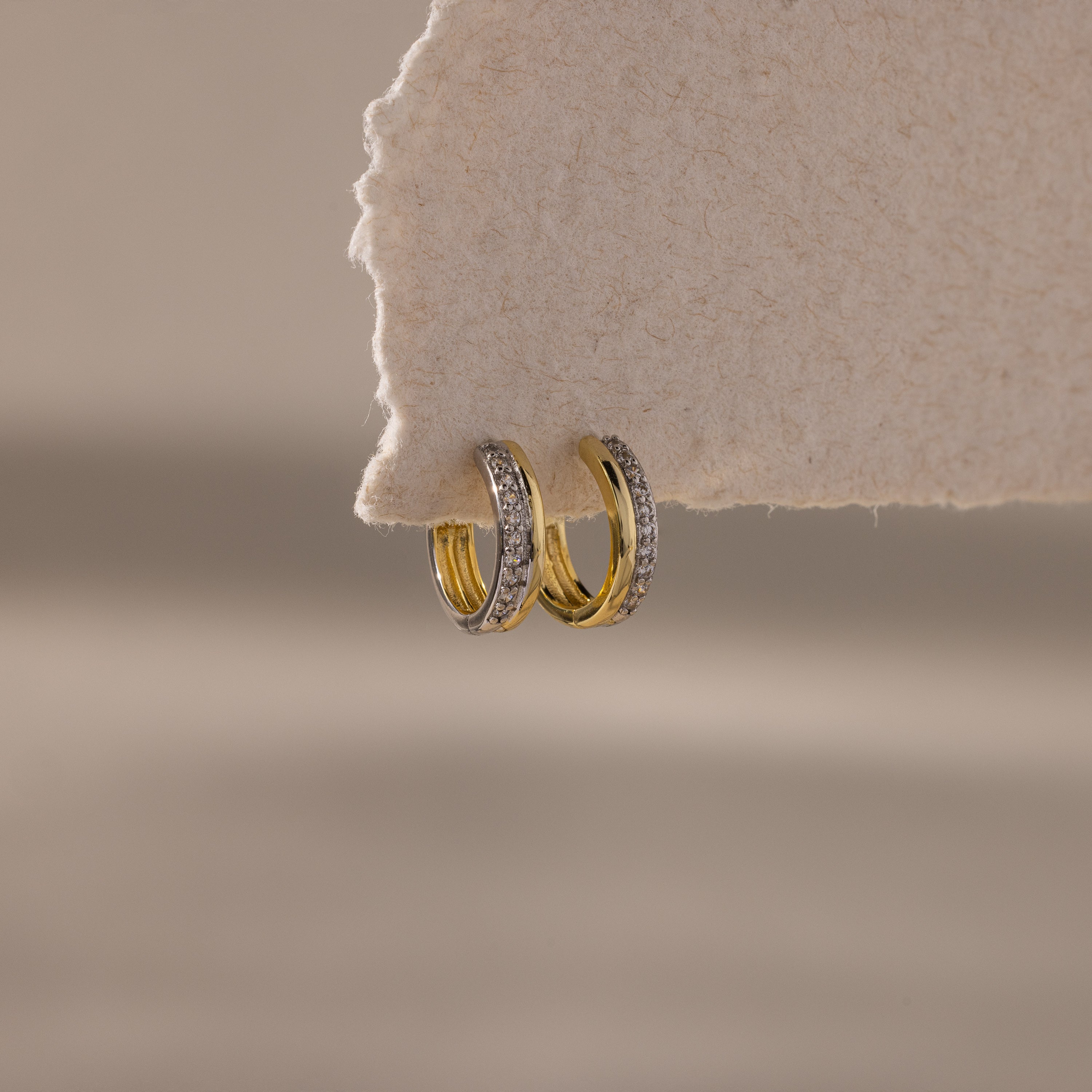 Two small Half Pave Huggies in Mixed Metal with embedded CZ diamonds hang on the edge of a textured, off-white surface.