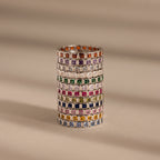 A stack of Eternity Bezel Birthstone Rings with square-cut gemstones in elegant bezel settings, arranged in rows on a beige surface with soft shadow lines.