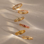 Six gold Eternity Bezel Garnet Rings with square cut garnet gemstones are arranged diagonally on a neutral background.