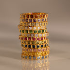 A stack of Eternity Bezel Birthstone Rings with square-cut gemstones in bezel settings is arranged in rows on a reflective surface.