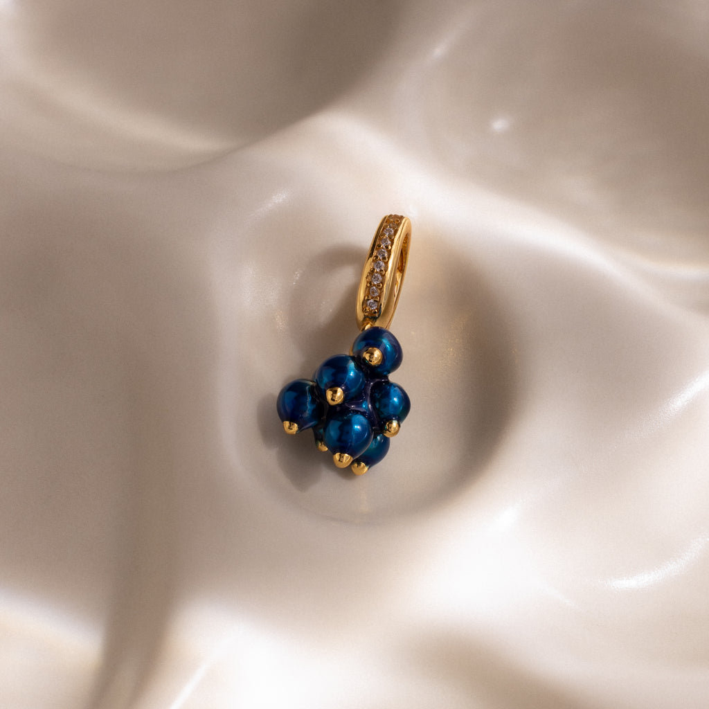 The Zircon Blueberry Charm features blue beads and pavé stones, beautifully displayed on a smooth, pearly white surface—a standout addition to our jewelry collection.
