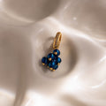 The Zircon Blueberry Charm features blue beads and pavé stones, beautifully displayed on a smooth, pearly white surface—a standout addition to our jewelry collection.