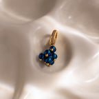 The Zircon Blueberry Charm features blue beads and pavé stones, beautifully displayed on a smooth, pearly white surface—a standout addition to our jewelry collection.
