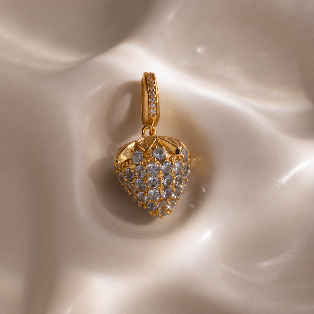 Aquamarine Blue Raspberry Charm with pavé stones and small clear gemstones on a smooth, cream-colored surface—a strikingly elegant piece to enhance any jewelry collection.