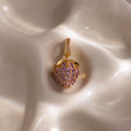 Pink Tourmaline Raspberry Charm—heart-shaped pendant with pavé stones and pink tourmaline gems, elegantly displayed on a silky, cream-colored surface. A refined addition to any jewelry collection.