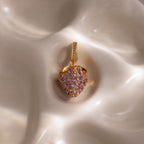 Pink Tourmaline Raspberry Charm—heart-shaped pendant with pavé stones and pink tourmaline gems, elegantly displayed on a silky, cream-colored surface. A refined addition to any jewelry collection.