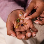 A hand displays six sparkling gold and gemstone charms, including the Alexandrite Peach Charm—a unique Birthstone Fruit Charm—alongside leaf and animal designs, each adorned with pavé stones for a dazzling jewelry collection addition.