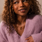 Smiling woman in a fuzzy lavender sweater with curly hair, wearing the Birthstone Fruit Charm necklace from a unique jewelry collection.