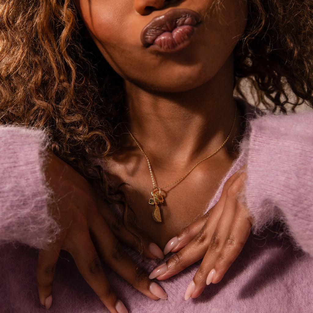 Woman with curly hair wears a Peridot Lime Charm necklace and a fuzzy lavender sweater, with her hands near her chest.