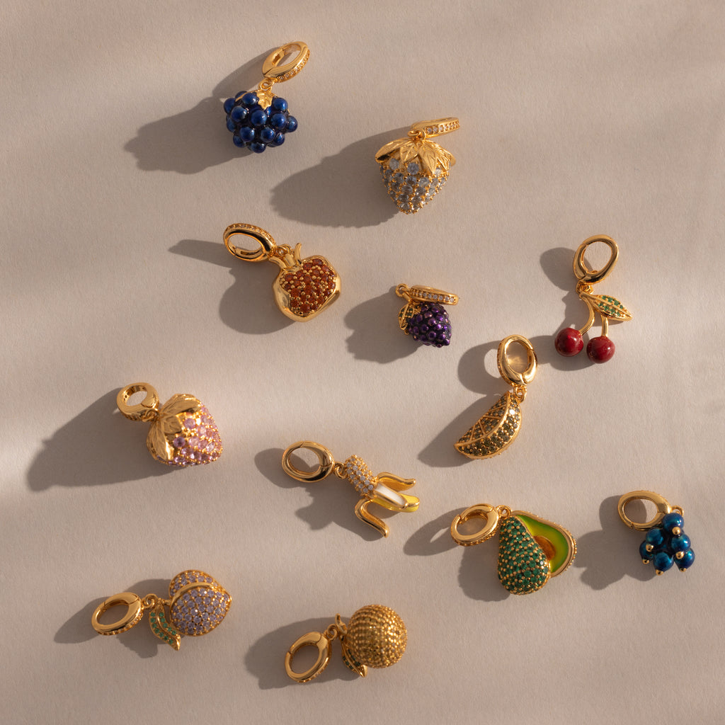 The Pink Tourmaline Raspberry Charm, adorned with pavé stones, is one of twelve gold and jeweled charms—like the Birthstone Fruit Charm and pea pod—making a delightful addition to any jewelry collection.