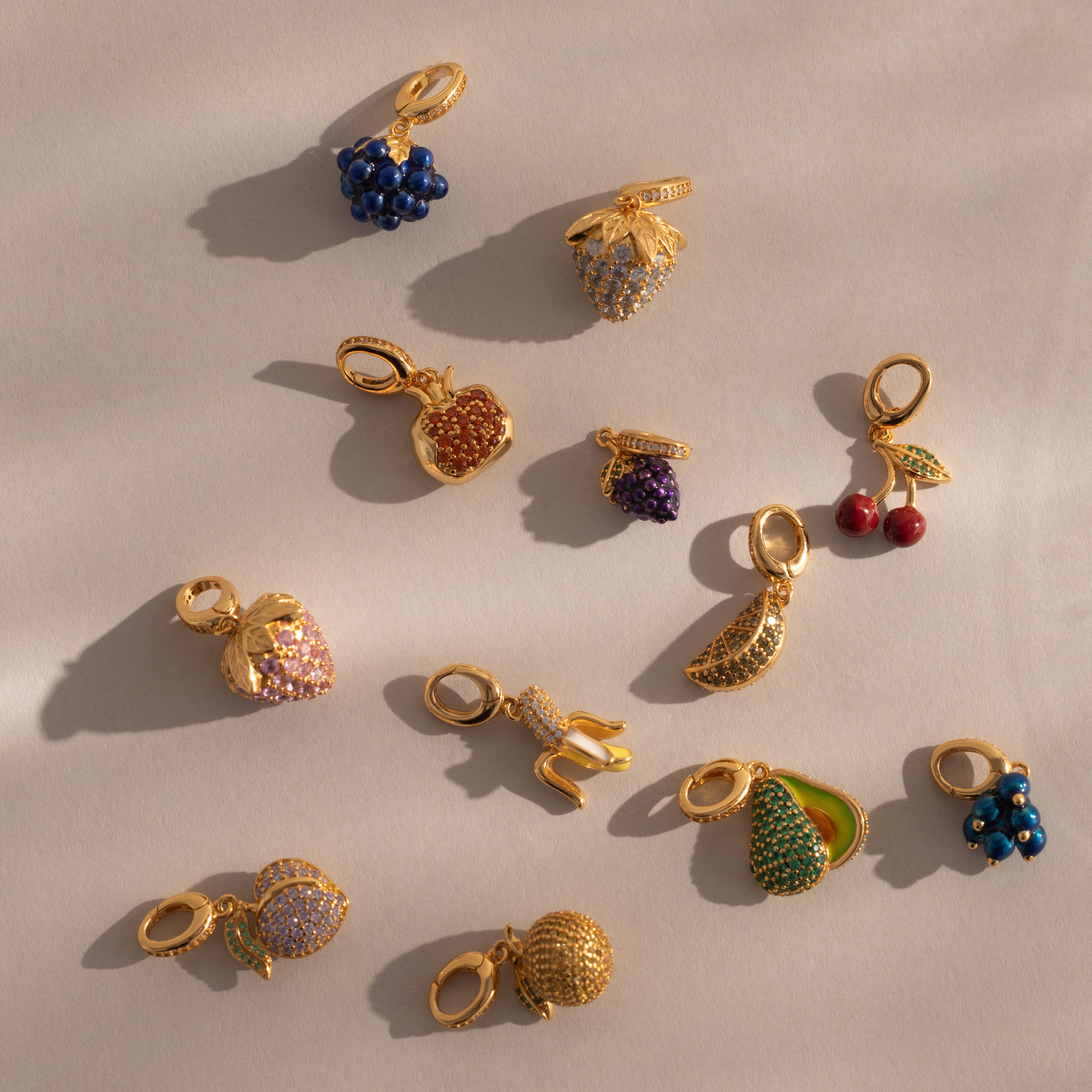 The Pink Tourmaline Raspberry Charm, adorned with pavé stones, is one of twelve gold and jeweled charms—like the Birthstone Fruit Charm and pea pod—making a delightful addition to any jewelry collection.