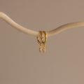 The Ericka Opal Huggies, featuring gold hoops with diamond-shaped pendants, hang on a curved branch—an elegant addition to any personalized jewelry collection.